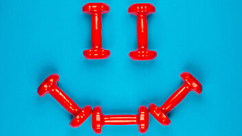 A smiley face made from red dumbbells on blue background, shot from above.