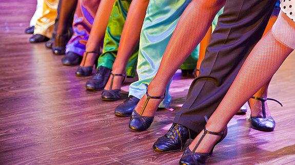 Man sieht viele Beine und Schuhe auf einer Tanzfläche. Alle sind Chick und Bunt angezogen.
