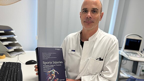 Dr. med. Jörg Streich hält das Buch zum Thema "Sport Injuries" in die Kamera